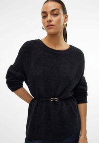 Zwarte textuurtrui met een ontspannen pasvorm, wijde halslijn en opgerolde mouwen, omgesnoerd op de taille met een zwarte riem met een gouden gesp.