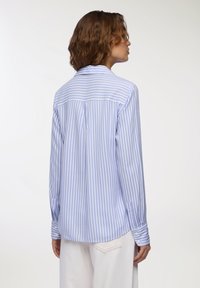 Camicia a righe blu e bianche con yoke posteriore, maniche lunghe, polsini con bottone e orlo curvo. Tessuto in misto cotone, texture liscia.