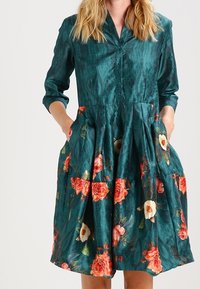 Teal floral dress with a button-down front, three-quarter sleeves, and pockets. Features pink and white roses, structured skirt with pleats.