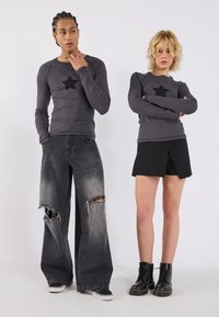 Hallide hall sleeves mustrid mustrid ja musta tähe aktsentidega, kombineeritud kulunud laiade teksade ja musta seelikuga, täiendab mustad saapad.
