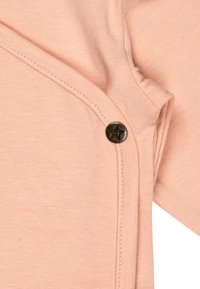 Peach-colored fabric with visible stitching and a black snap button featuring a star-shaped embossment near the seam.