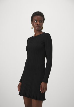 Black ribbed knit dress with long sleeves, featuring a crew neckline and a flared hem with a ruffled edge. Smooth texture.