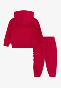 Red hoodie and matching sweatpants set made from soft material. Hoodie features a hood, while pants have an elastic waistband and side logo.