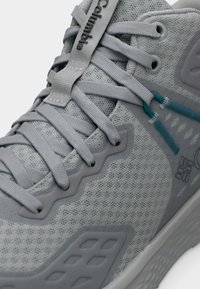 Κοντινή λήψη γκρι αθλητικού παπουτσιού με υφασμάτινο πλέγμα υφής, παχιά σόλα και σφιχτά δεμένα επίπεδα γκρι κορδόνια με τιρκουάζ αγκράφες.