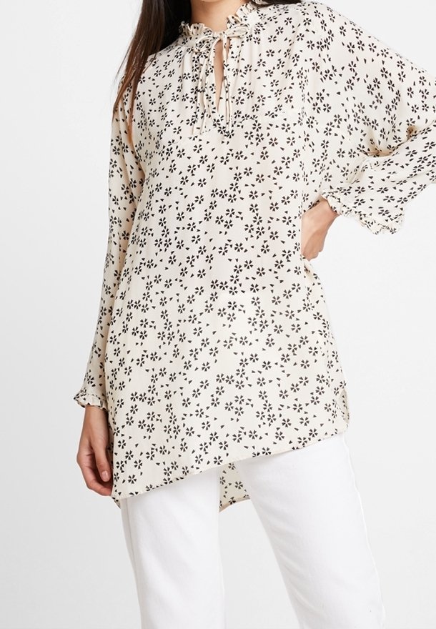 Kukkakuosiset vaaleankermanväriset paita mustilla kuvioilla, jossa on avainaukko-solmukiinnitys, pitkät hihat ja rento malli. Yhdistetty valkoisiin housuihin.