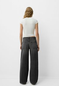 Široke črne kavbojke iz denima z zadnjimi žepi, v kombinaciji s prilegajočo belo majico. Tkanina je mehka z rahlo zbledelim videzom.