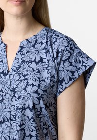 Blusa con motivo floreale in azzurro chiaro con fiori blu scuro, maniche corte, scollatura a V e tessuto dalla texture liscia.
