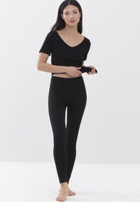 Zwarte korte mouwen top met een V-hals, gecombineerd met zwarte leggings. Beide items zijn nauwsluitend, rekbaar en gemaakt van een gladde stof.