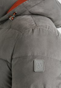 Graue gepolsterte Jacke mit einer glatten, weichen Textur. Verfügt über ein oranges Innenfutter und ein graues Logo-Patch am Ärmel.