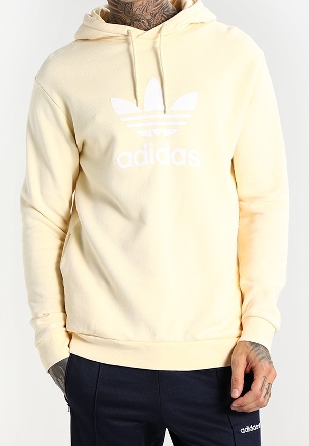 Žlutá mikina z měkkého materiálu, se bílým logem Adidas a třemi pruhy přes hruď. Kapuce se stahovací šňůrkou a žebrované manžety.