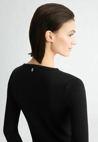 Top nero a maniche lunghe con un design aderente, texture a coste e un piccolo logo ricamato sul retro del collo.