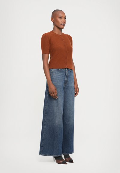 Brown short-sleeve cardigan with button closure, paired with wide-leg blue jeans and black pointed-toe heels, on a plain background.