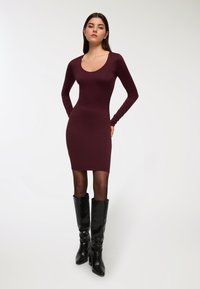 Bordo długa rękawowa sukienka bodycon z okrągłym dekoltem, miękka faktura, dopasowany krój, w połączeniu z wysokimi czarnymi skórzanymi botkami na obcasie.