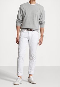 Grauer Baumwoll-Sweatshirt, weiße Jeans, braumer Leder Gürtel und weiße Sneaker. Aufgerollte Ärmel und ein kleines Logo auf der Brust. Legere Kleidung.