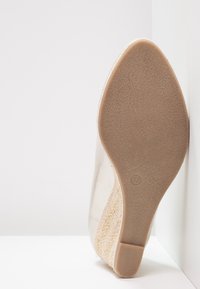 Chaussure à talon compensé beige avec une semelle texturée, un dessus lisse et un accent doré. Taille indiquée comme 37 sur la semelle.