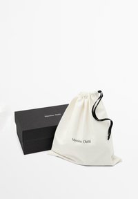 Zwarte rechthoekige doos en witte trekkoordzak met zwarte koord, beide gelabeld met "Massimo Dutti" op een effen witte achtergrond.