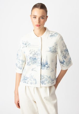 Short-sleeve button-up shirt in off-white linen featuring blue botanical prints. Structured collar, relaxed fit, and a slightly cropped hem.