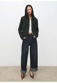 Czarna, krótka marynarka z tweedu z złotymi guzikami, zestawiona z ciemnoniebieskimi jeansami o szerokich nogawkach z podwiniętymi brzegami oraz brązowymi butami o ostrym nosku.