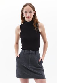 Zwarte mouwloze top met een neklijn, gecombineerd met een grijze wollen rok met zijzakken en een ceintuur in de taille.