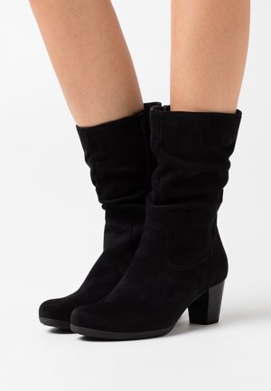 Bottines en suède noir avec un design décontracté, bout rond et un talon carré de 3 pouces. Fermeture éclair sur le côté pour un enfilage facile.