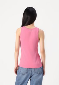 Top sin mangas rosa hecho de un tejido suave, con un escote redondo y un corte ajustado, combinado con pantalones vaqueros azules.