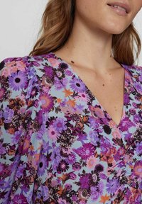 Blommig klänning med lila, rosa och orange blommor på en ljusblå bakgrund. V-ringad design med skräddade ärmar och tygtextur.