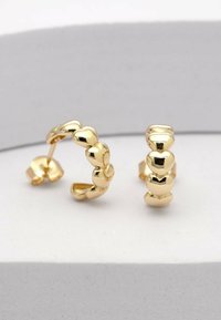 Goldene Creolen mit herzförmigen Designs entlang des Rings. Die glatte Textur und die reflektierende Oberfläche steigern die visuelle Anziehungskraft.