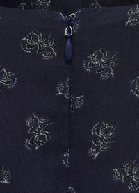 Tessuto navy con un motivo floreale in grigio e bianco, dotato di una cerniera centrale con un tirante navy e dettagli di cucitura sottili.