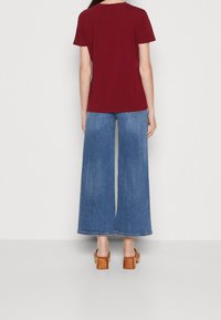 Burgundowa koszulka połączona z szerokimi dżinsami w kolorze niebieskim. Outfit dopełniony jest brązowymi sandałami na obcasie. Prosty design i luźny krój.