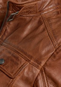 Bruine leren jas met een gestructureerd oppervlak, voorzien van een zilveren rits, gestikte accenten en een klepzakdetail.