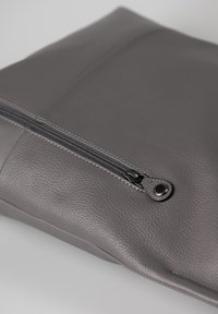Borsa in pelle grigia con finitura texturizzata, dotata di zip superiore e cuciture in contrasto lungo la cucitura. Forma rettangolare compatta.