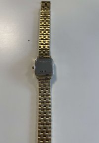 Reloj de pulsera de metal dorado con caja cuadrada, diseño de pulsera trenzada y parte trasera pulida en plata que muestra "ROSEFIELD AM NYC" y la marca CE.