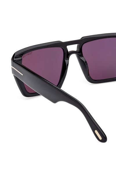 Black sunglasses with a geometric frame, dark purple lenses, and a matte black temple featuring a metal accent near the hinge.