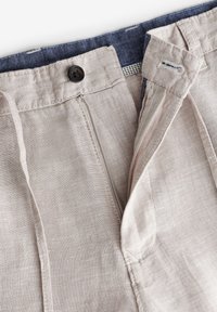 Pantaloni in lino beige con zip, chiusura con bottone superiore e vita blu. Presentano una finitura sottile e tasche laterali.