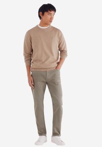 Maglione beige, pantaloni grigi chiari e sneakers bianche. Tessuto morbido, design a collo rotondo, polsini a coste, vestibilità casual. Stile minimalista con linee pulite.