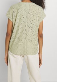 Haut vert clair à manches courtes avec motif ajouré et ourlet festonné. Confectionné dans un tissu respirant, il présente une coupe décontractée et un col rond.