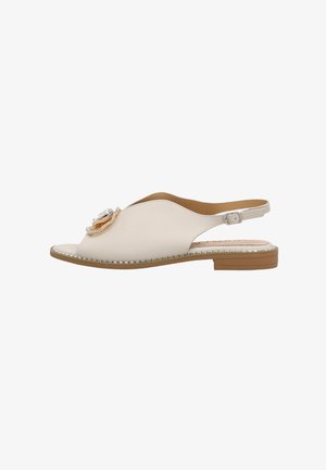 Beżowa płaska sandałka z odkrytymi palcami i paskiem z tyłu, ozdobiona kwiatem oraz srebrną dekoracją z koralików wzdłuż krawędzi podeszwy.