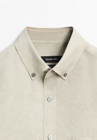 Colletto beige di camicia con tre bottoni visibili ed etichetta del marchio "Massimo Dutti" all'interno dello scollo.