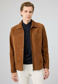 Bruine suède jas met een licht gestructureerde kraag, ritssluiting, twee zijzakken en een gladde textuur, gedragen over een donker polo-shirt.