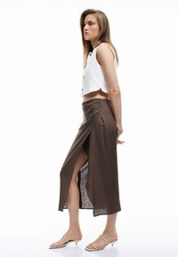 Hvid cropped tanktop med rund kant og knapdetalje, parret med en brun maxikjole med en forskydning foran og samlet side tekstur.