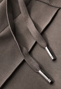 Tessuto marrone con una superficie texture, dotato di lacci piatti e puntali in metallo argentato. I lacci sono morbidi e sembrano ben cuciti.