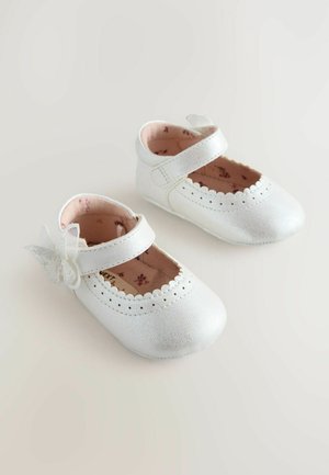 Zapatos para bebés de cuero blanco con borde acanalado, correa al tobillo y un adorno decorativo de mariposa. Forro suave en rosa con estampado floral.