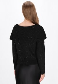 Schwarzer Pullover mit weitem, geripptem Ausschnitt und einem strukturierten Muster. Funkelnde Akzente sorgen für einen dezenten Glanz. Lange, eng anliegende Ärmel.