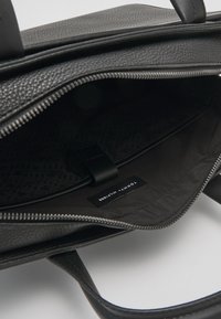 Sac en cuir noir avec extérieur texturé, fermeture éclair et intérieur à motif. Comprend une étiquette de marque et une sangle intérieure pour l'organisation.