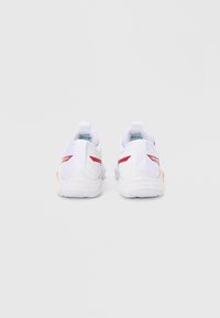 Ζεύγος λευκών αθλητικών παπουτσιών με κόκκινες λεπτομέρειες, εμφανιζόμενα από πίσω, σε απλό λευκό φόντο.