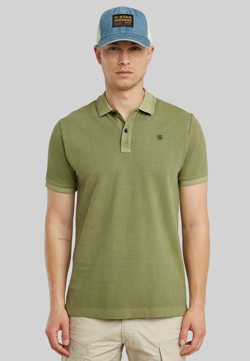 Polo shirt verde oliva con una pattina a tre bottoni, maniche corte e colletto a contrasto. Piccolo logo sul petto. Tessuto leggero.