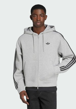 Felpa grigia con zip realizzata in un misto cotone. Presenta strisce nere sulle maniche e un logo ricamato nero sul petto.