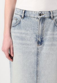 Lyseblå denimskjørt med rett snitt, med mørk søm, mid-rise livlinning og frontlommer. Tøyet har en glatt tekstur.