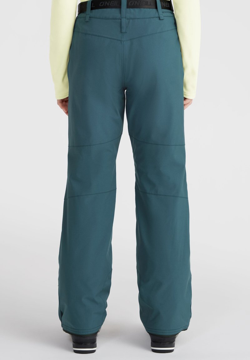 Türkisfarbene, wasserdichte Schneehosen mit lockerer Passform, verstellbarem Bund und gesteppten Paneeldetails; kombiniert mit schwarzen Skischuhen.