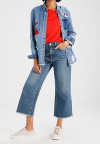 Jeanshemd mit Stickerei, rotop, weit geschnittene Jeans mit ausgefranstem Saum, beige Sneakers. Lässige Kleidung mit lockerer Passform und kräftigen Farben.